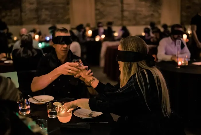 Bord med deltagere, der morer sig med Blingo under en Dinner in the Dark teambuilding, hvor samarbejde og kommunikation udfordres i mørke omgivelser