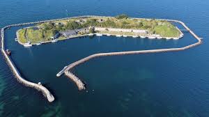 Luftfoto af Flakfortet, en ø-fæstning med grønt areal og havnemole i Øresund.