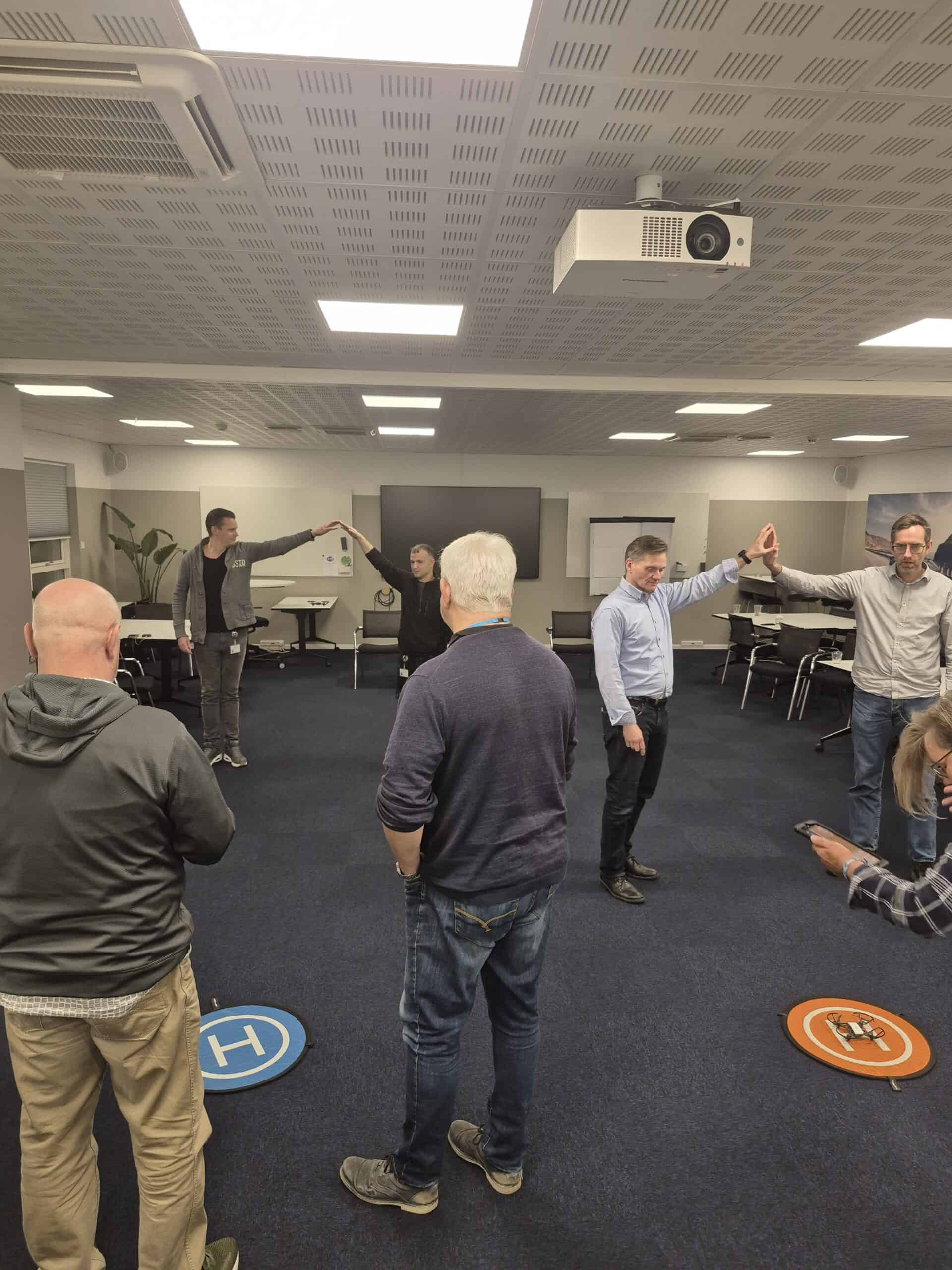 Personer danner bue med armene over drone landingsmåtter under teambuilding.