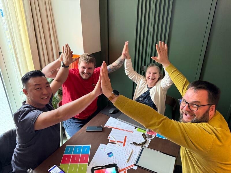 Glad gruppe på fire personer, der giver high-five under teambuilding.