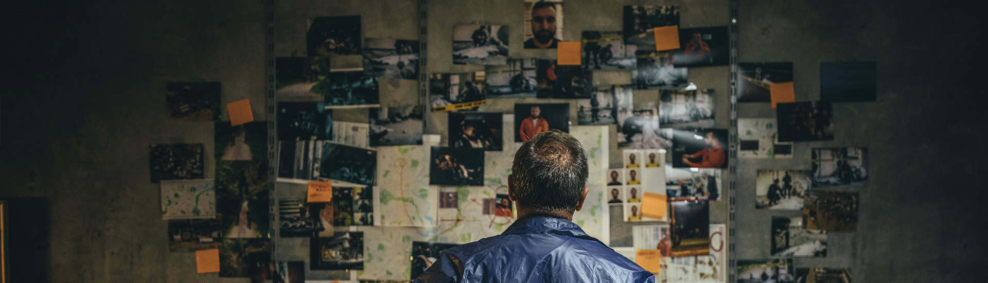 Mand betragter efterforskningsvæg med billeder og noter.